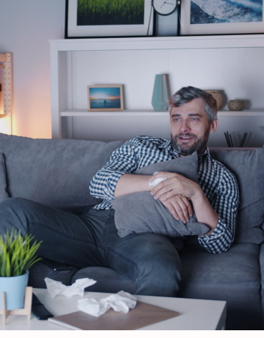 Mental sundhed og anti-stress: Middelaldrende mand der sidder i en sofa og krammer en pude mens han ser fjernsyn